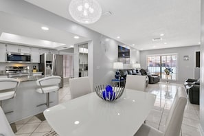 A modern kitchen with stainless steel appliances, a dining area with a white table, and a living room with leather sofas.