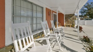 A covered outdoor seating area with white chairs and a stone wall. - Tampa's Paradise (Tampa)
