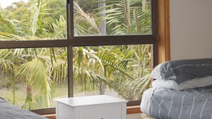 A bedroom with a large window, a bed with gray bedding, and a white bedside table. - Beach House in the Ulladulla Mollymook Milton area (Ulladulla)