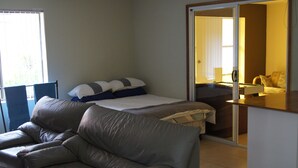 A room with a bed, a sofa, a desk, and a sliding door leading to another room. - Beach House in the Ulladulla Mollymook Milton area (Ulladulla)