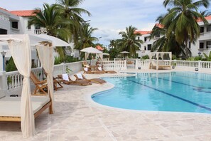 A poolside area with lounge chairs and umbrellas, surrounded by palm trees and a white building with a red roof. - VAIA HOTELES (Coveñas)