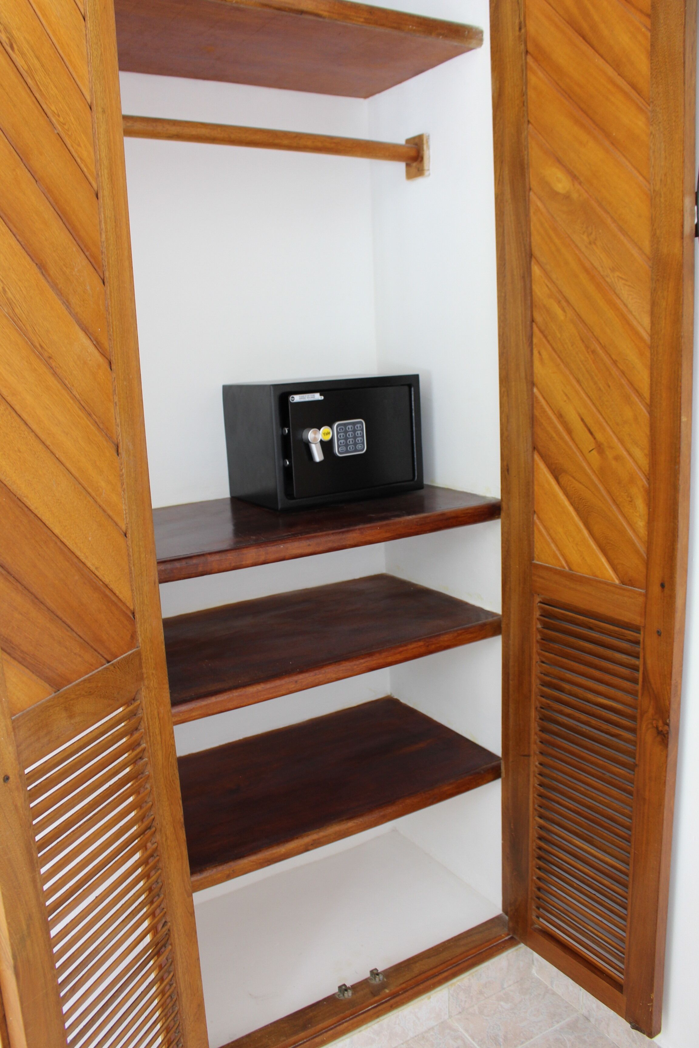 A wooden closet with a black safe on the top shelf.