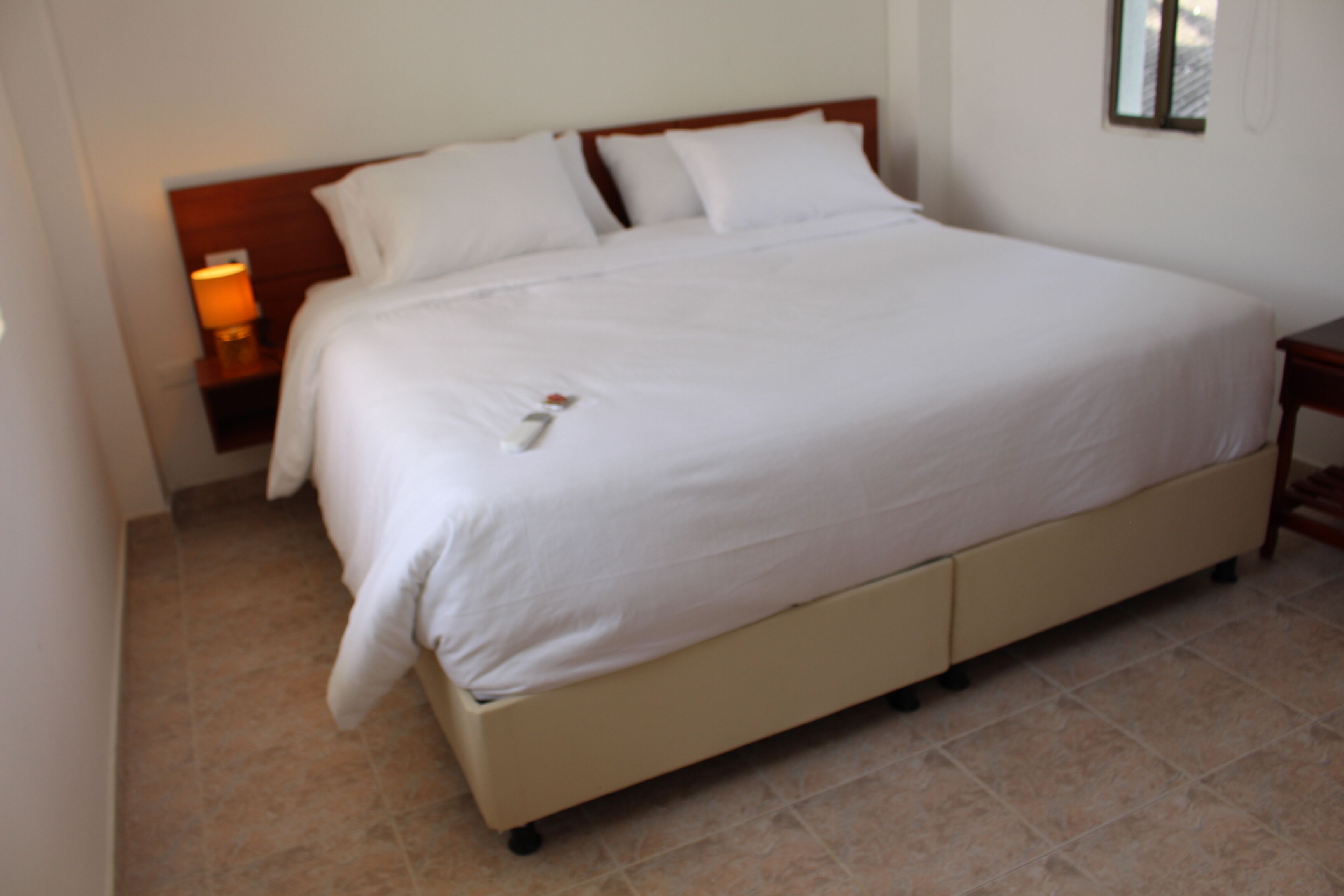 A large bed with white linens, a wooden headboard, and a bedside table with a lamp.