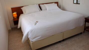 A large bed with white linens, a wooden headboard, and a bedside table with a lamp.