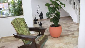 Una silla de madera con acabado envejecido, una planta en maceta y faroles decorativos en una habitación con piso a cuadros y paredes blancas.