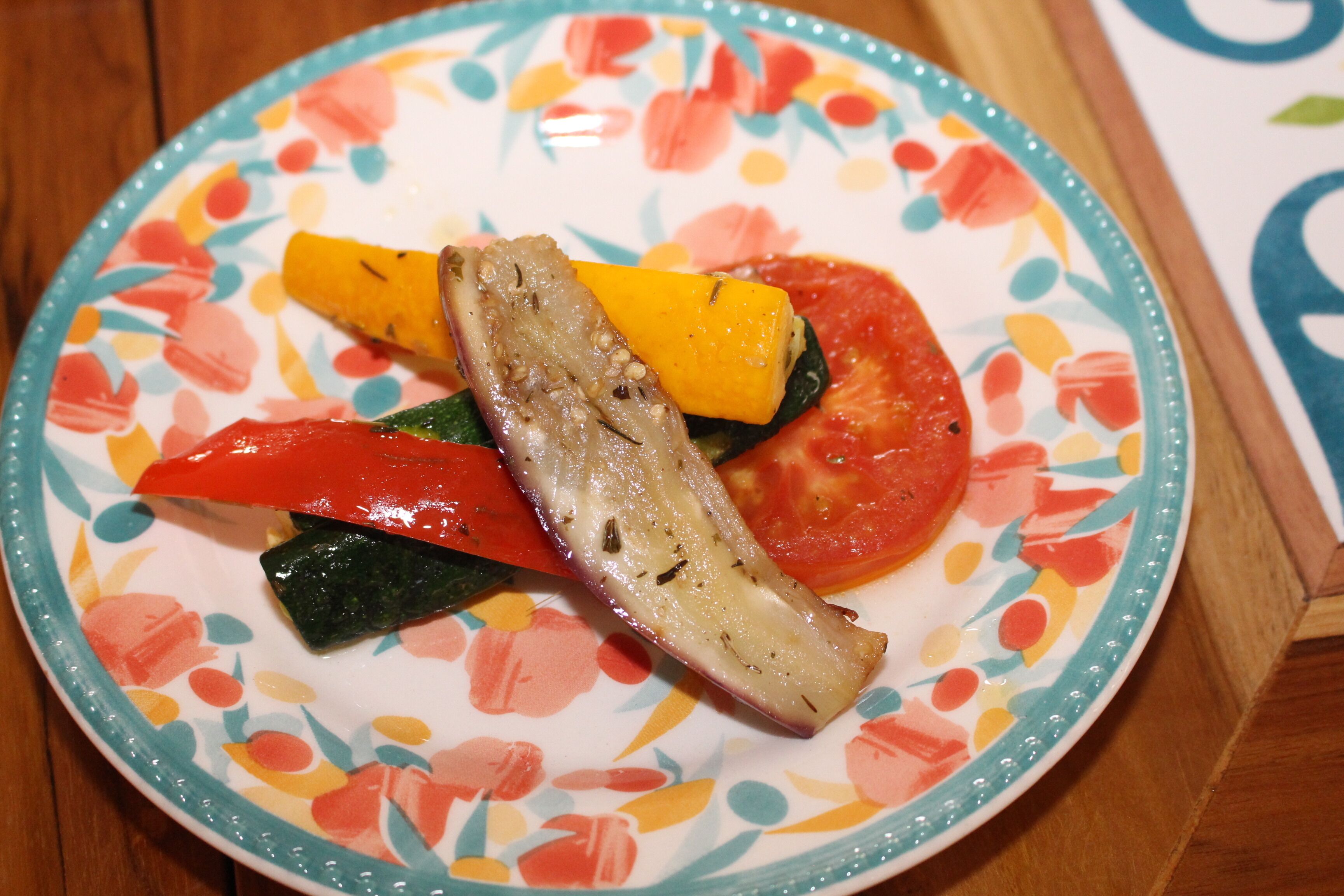 A plate with a colorful floral pattern and a variety of vegetables including tomatoes and squash.