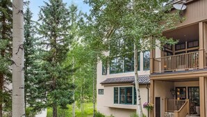 A two-story building with a stone pathway leading to a wooden deck, surrounded by trees. - Elegant Beaver Creek Retreat (Beaver Creek)