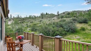A wooden deck with a table and chairs, overlooking a hilly landscape with greenery. - Elegant Beaver Creek Retreat (Beaver Creek)