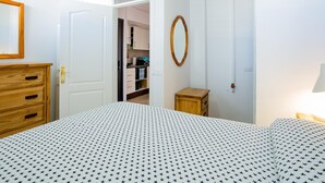 A bedroom with a bed, a wooden dresser, a wardrobe, and a small table.