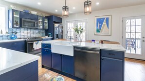 A modern kitchen with dark blue cabinets, a white countertop, and a large island. There are two pendant lights hanging above the island.
