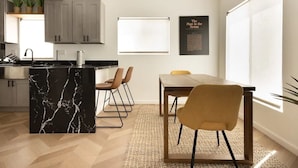 Une cuisine moderne dotée d’un îlot en marbre, de meubles gris et d’un coin repas avec une table et des chaises en bois.