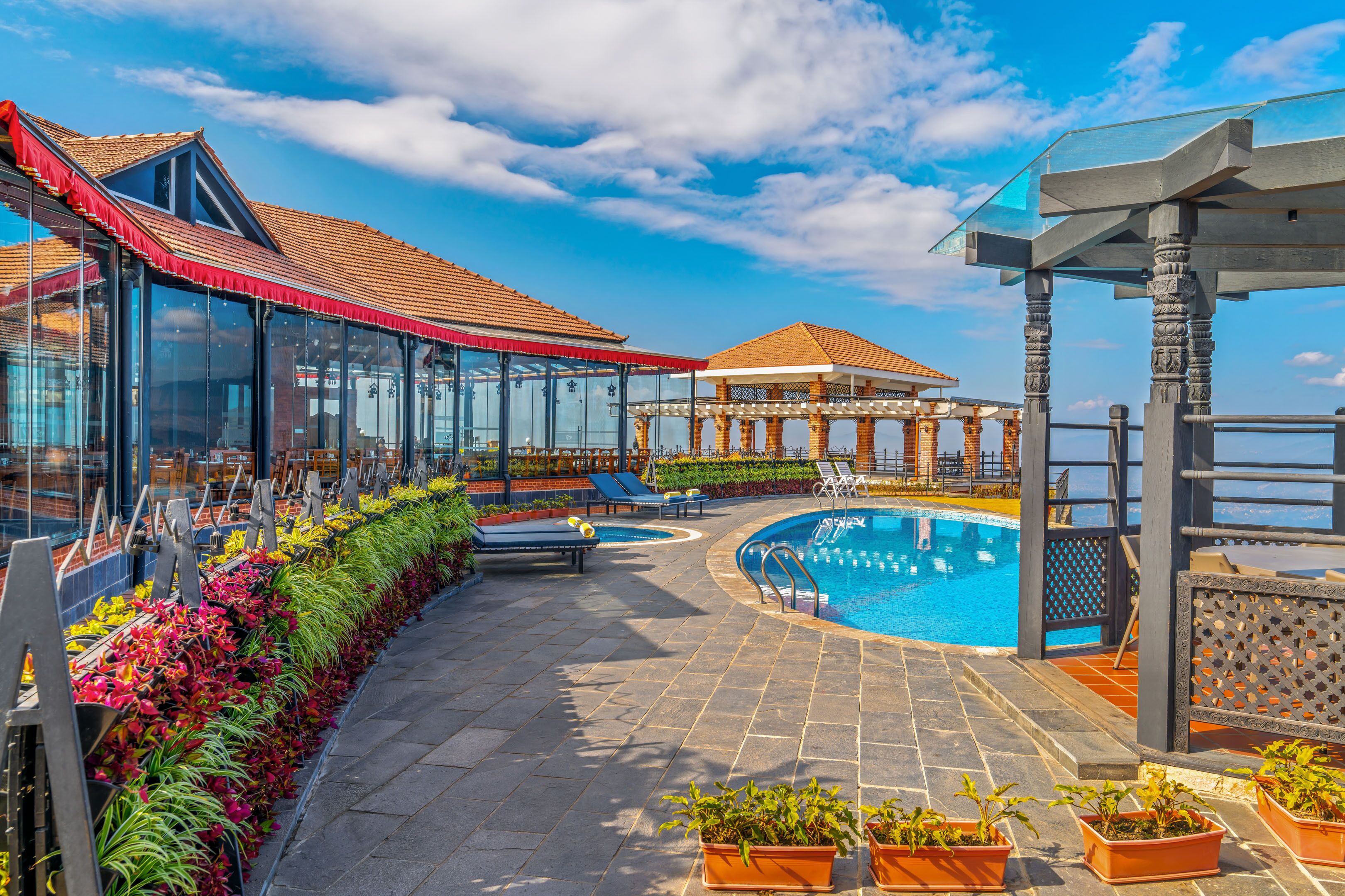 A pool area with a glass-enclosed lounge, a gazebo, and a view of the sea.