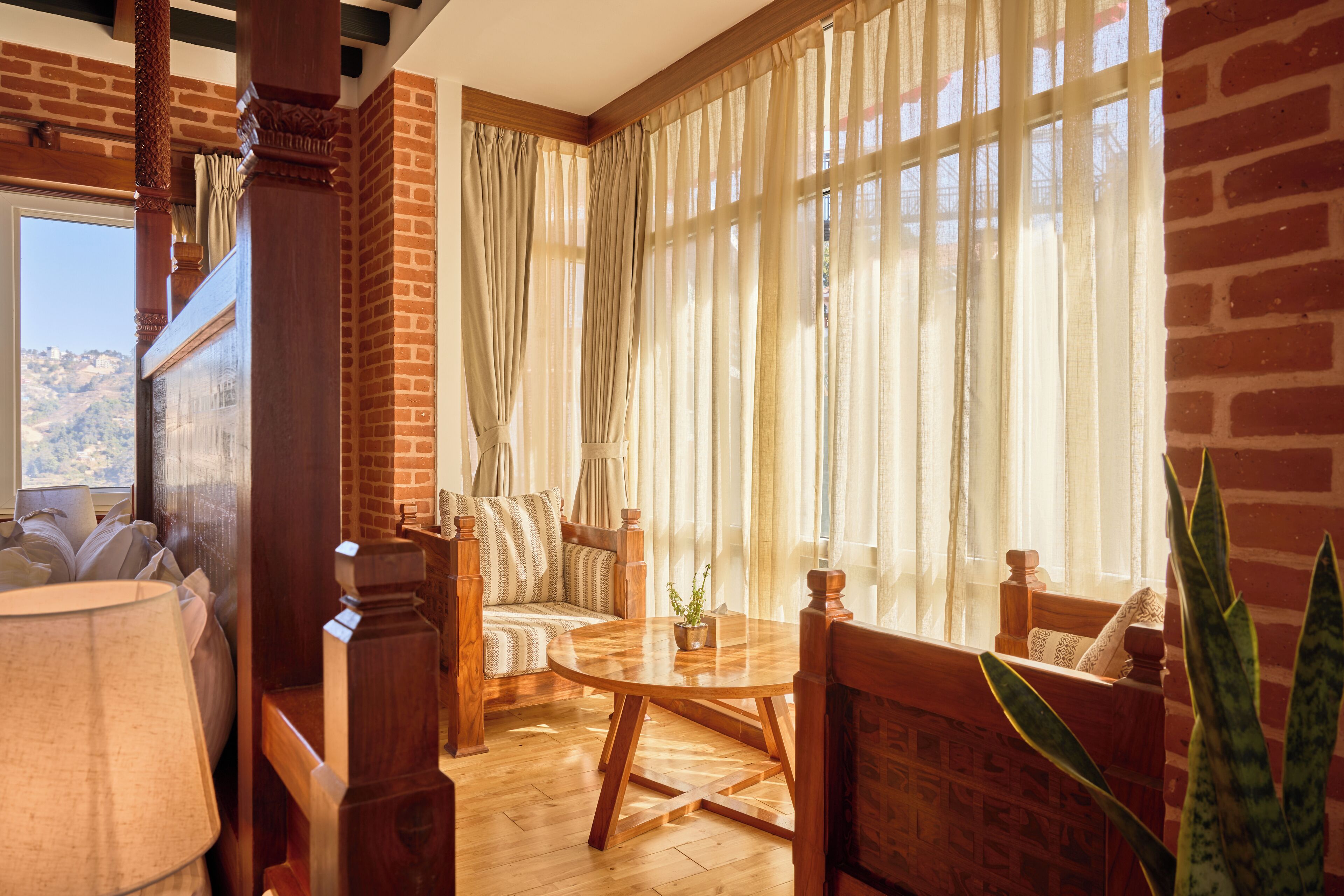 A cozy room with a brick wall, a wooden sofa, a round wooden table, and a large window with sheer curtains.