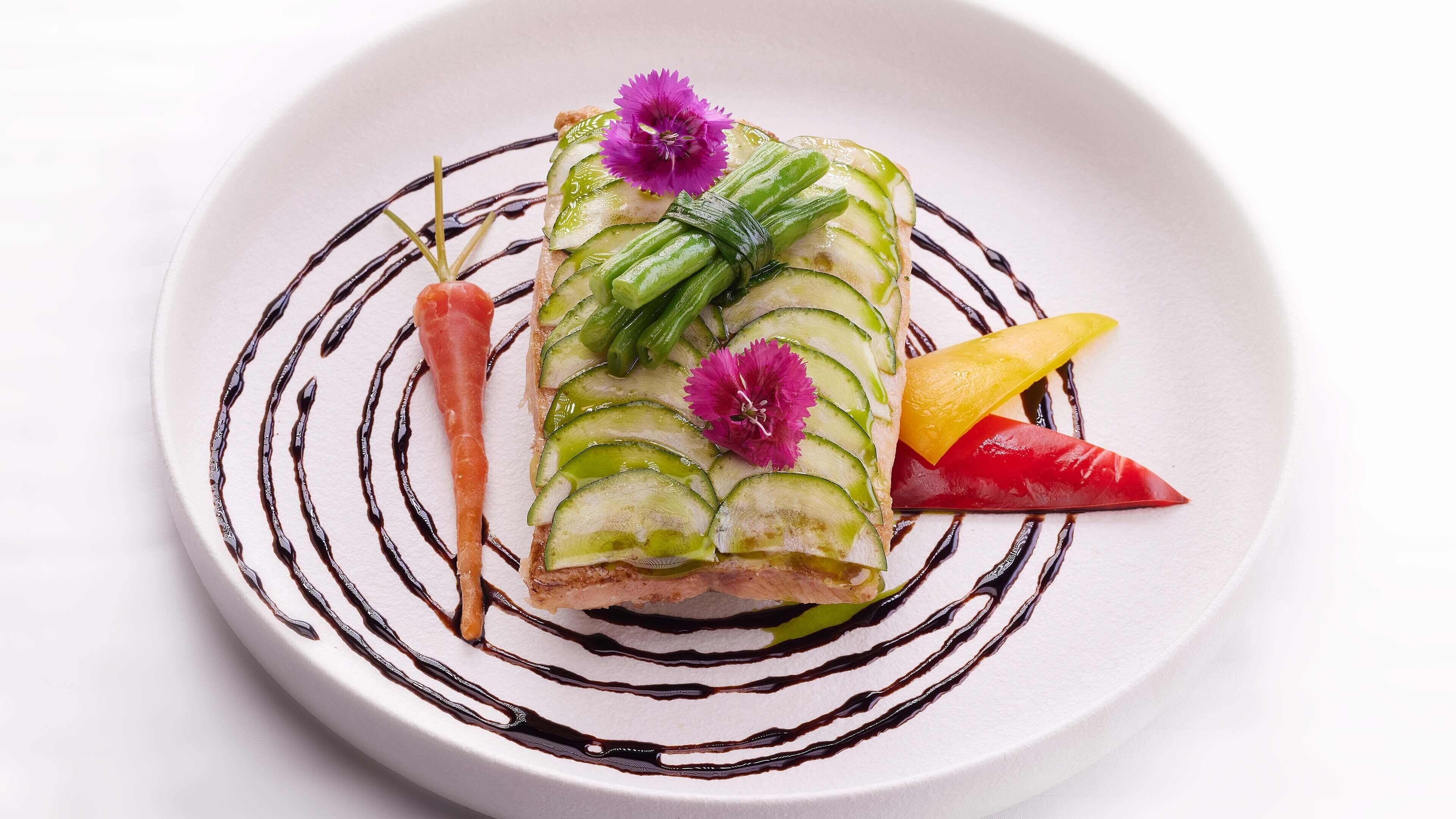 Un plato blanco con un diseño espiral negro, con rodajas de pepino, una zanahoria y un chile rojo.