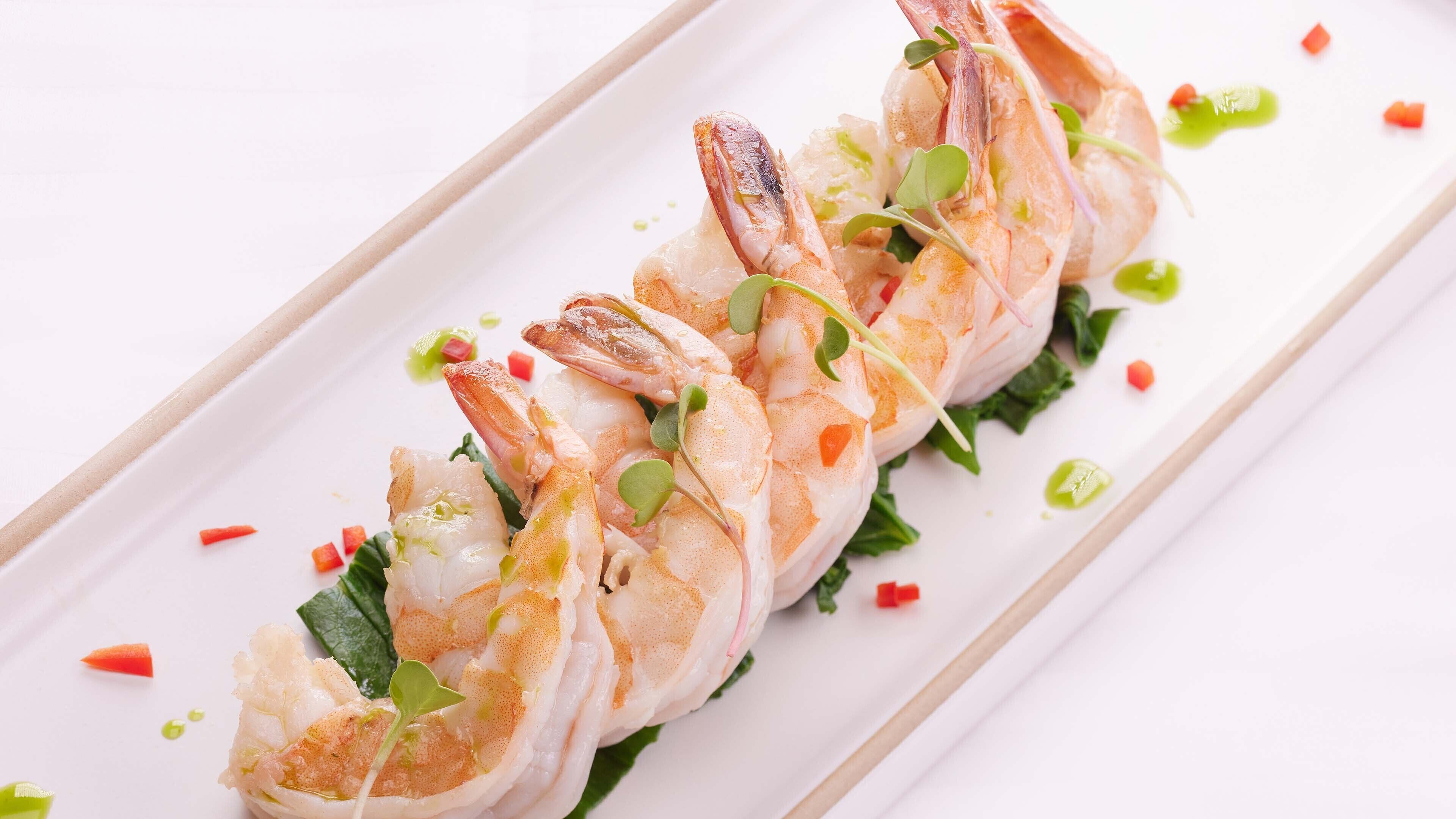 A dish of shrimp on a white plate with green leaves and red pepper.