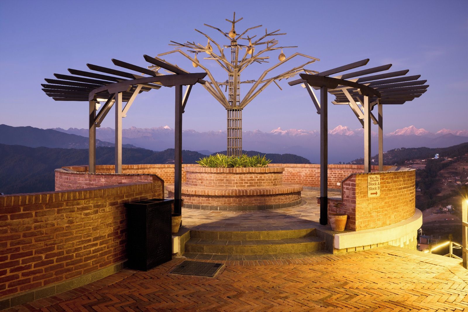 Una terrazza sul tetto con una scultura in metallo, pareti in mattoni e vista sulle montagne lontane.