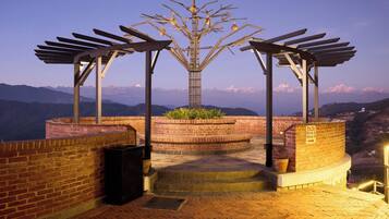 Una terraza en la azotea con una escultura metálica, paredes de ladrillo y vistas a montañas distantes.