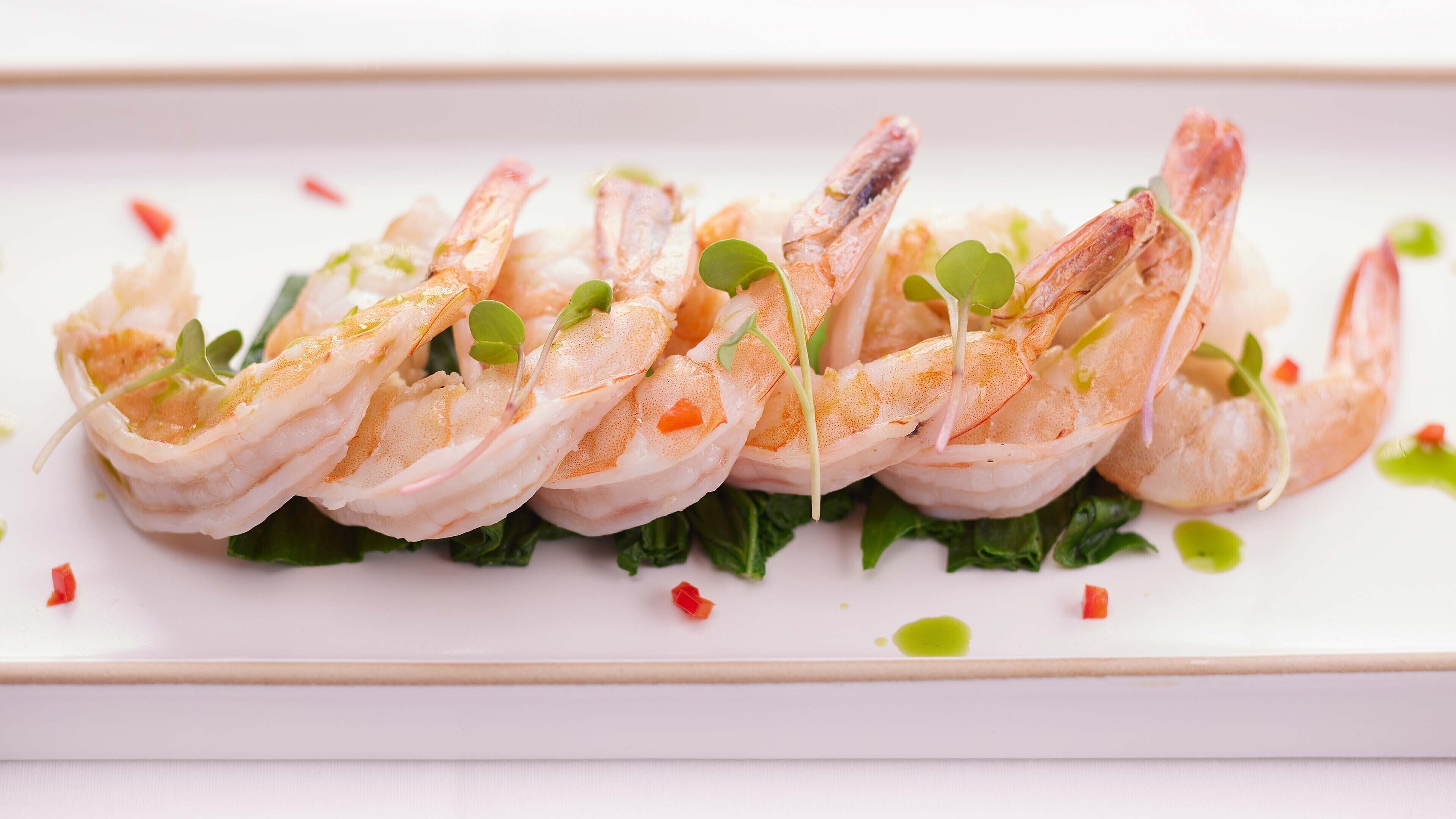 Une assiette de crevettes cuites, disposées en rangée sur un lit de verdure.