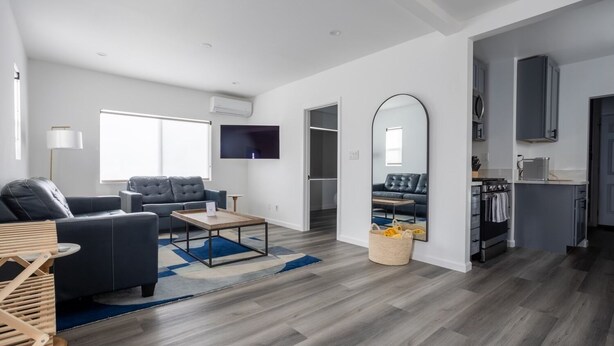 A modern living room with a grey sofa, a coffee table, and a TV mounted on the wall. - NEWLY RENOVATED BUNGALOW WITH FREE PARKING ON SITE (Los Angeles)