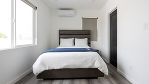 A modern bedroom with a dark headboard, white bedding, and a blue accent throw. - NEWLY RENOVATED BUNGALOW WITH FREE PARKING ON SITE (Los Angeles)