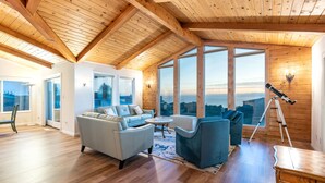 A spacious living room with a high ceiling, wooden beams, large windows, a telescope, and a cozy seating area. - Spacious * Ocean View * Walking Trail to Beach * Hot Tub (Bodega Bay)