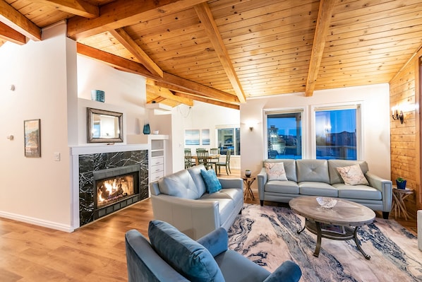 A spacious living room with a fireplace, leather sofas, a dining area, and large windows.