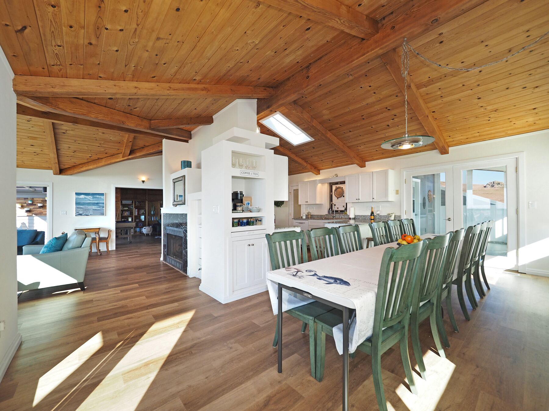 Un salón espacioso con techo de madera, una mesa de comedor con sillas y una zona de cocina con armarios blancos.