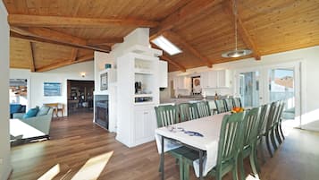 Un salón espacioso con techo de madera, una mesa de comedor con sillas y una zona de cocina con armarios blancos.