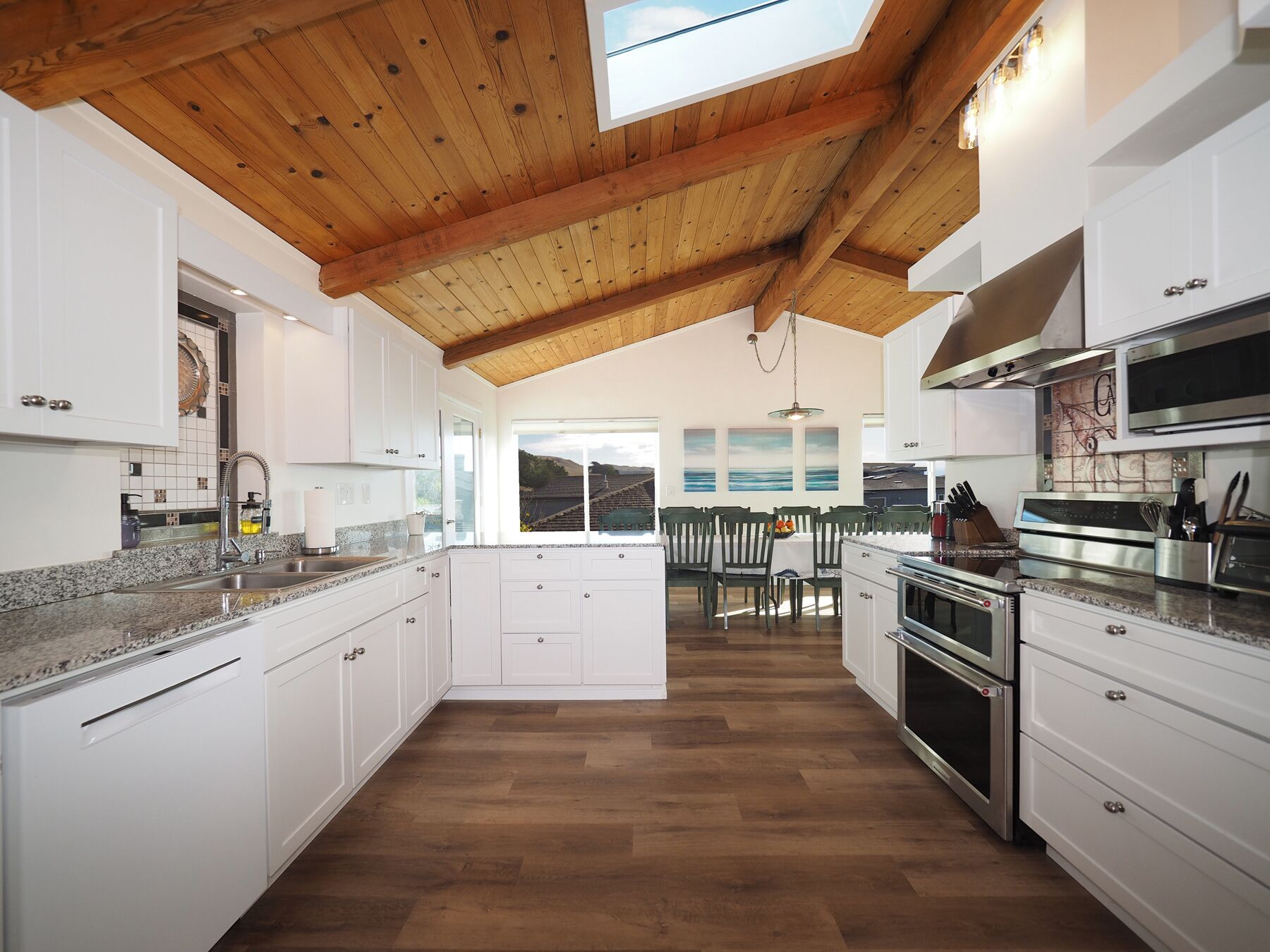 Una cocina moderna con armarios blancos, techo de madera y vistas a un comedor.
