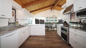 A modern kitchen with white cabinets, a wooden ceiling, and a view of a dining area. - Spacious * Ocean View * Walking Trail to Beach * Hot Tub (Bodega Bay)