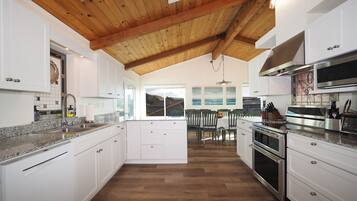 Una cocina moderna con armarios blancos, techo de madera y vistas a un comedor.