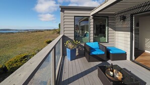 A modern outdoor deck with a clear view of the landscape, furnished with wicker furniture and a glass balustrade. - Spacious * Ocean View * Walking Trail to Beach * Hot Tub (Bodega Bay)