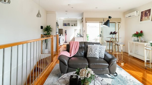 A modern living room with a leather sofa, a coffee table with flowers, and a staircase with a wooden railing. - Design/bright/cosy townhouse between airport &city (Glenroy)