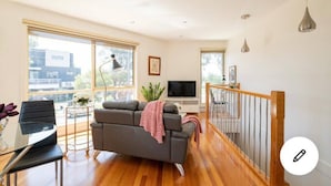 A modern living room with a grey sofa, a TV, and a dining area with a table and chairs. - Design/bright/cosy townhouse between airport &city (Glenroy)
