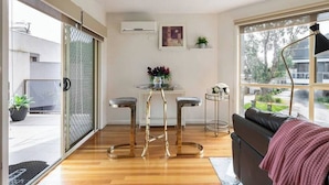 A modern living room with a sliding glass door, a black leather sofa, a round coffee table, and a bar stool set. - Design/bright/cosy townhouse between airport &city (Glenroy)