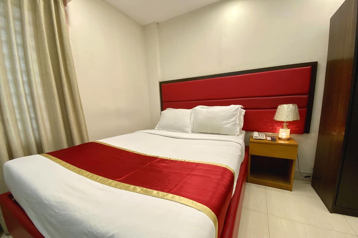 A hotel room with a large bed, a red headboard, white bedding, a bedside lamp, and a wooden nightstand.