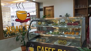Una cafetería con una vitrina de vidrio llena de frutas y una persona lavando platos.