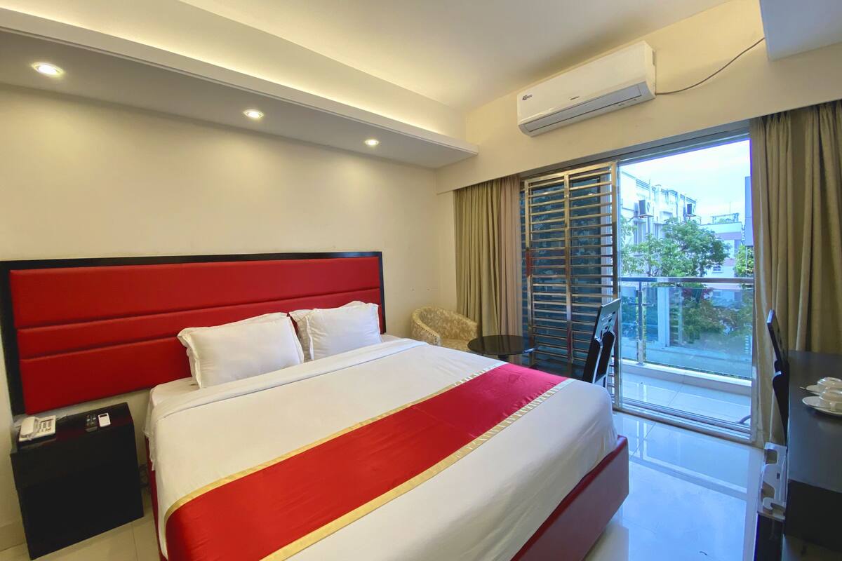 A hotel room with a large bed, a bedside table, a chair, a desk, and a window with curtains.