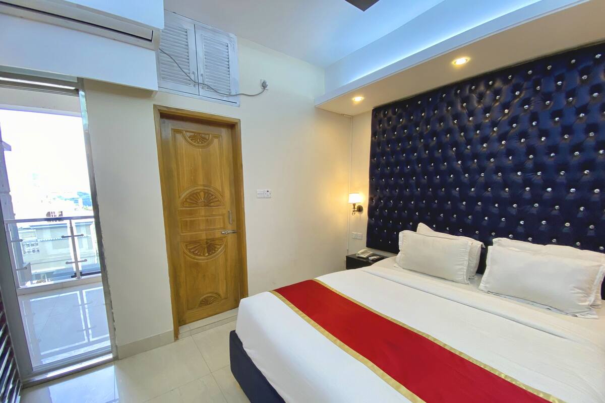 A hotel room with a bed, a wooden door, a window, and a balcony.