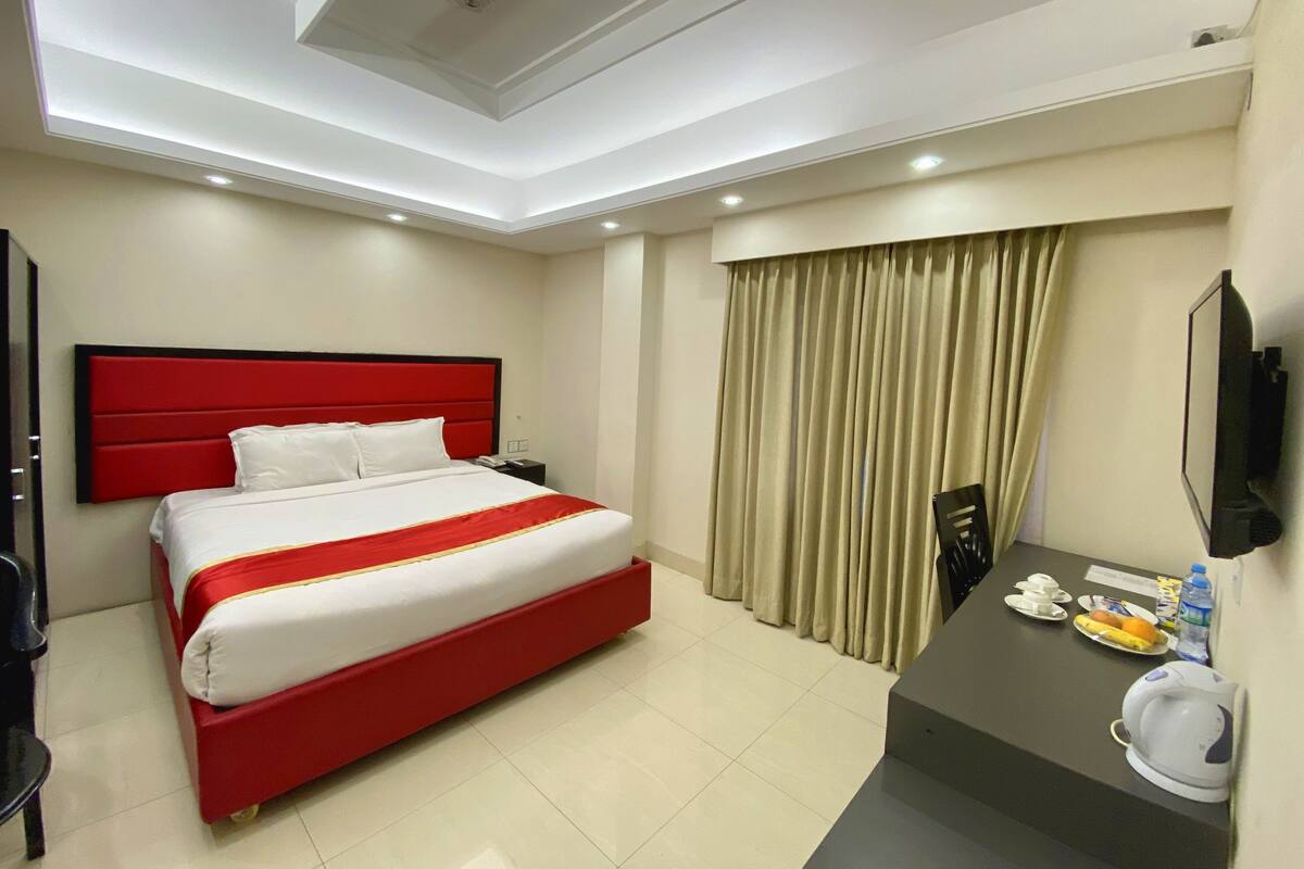 A hotel room with a red bed, a desk with a telephone, and a television on the wall.
