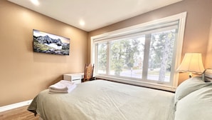 A bedroom with a bed, a nightstand, a lamp, a window with a view of trees, and a painting on the wall. - Renovated Rooms 10-min to Finch Subway Near Yonge St (Toronto)