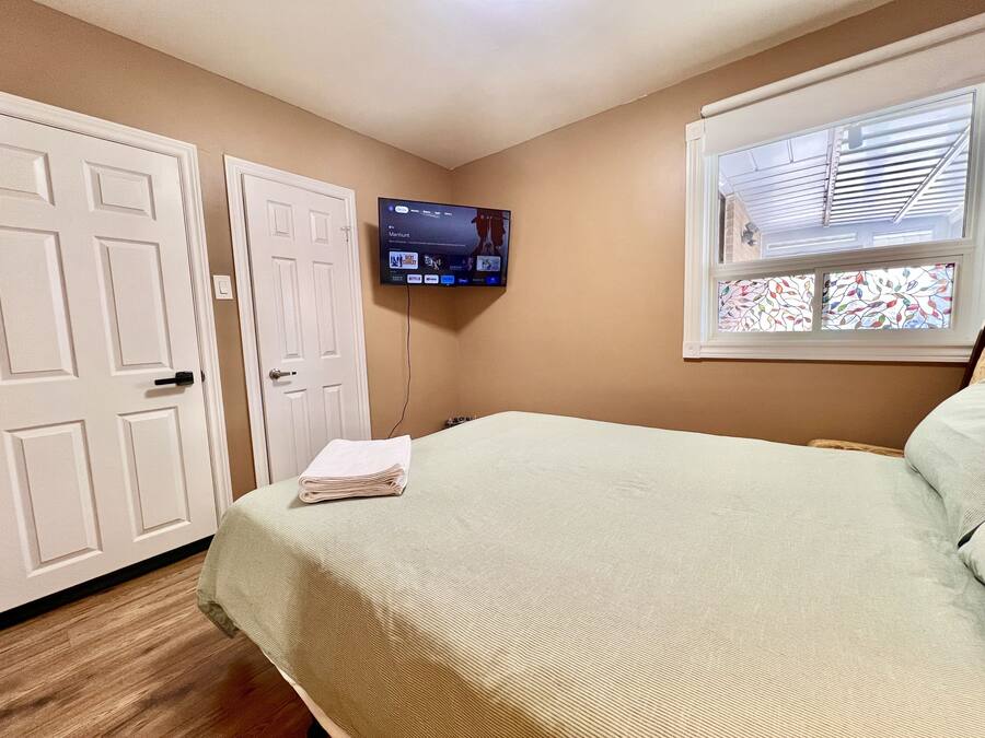 Een slaapkamer met een bed, een aan de muur bevestigde televisie en een raam met jaloezieën.