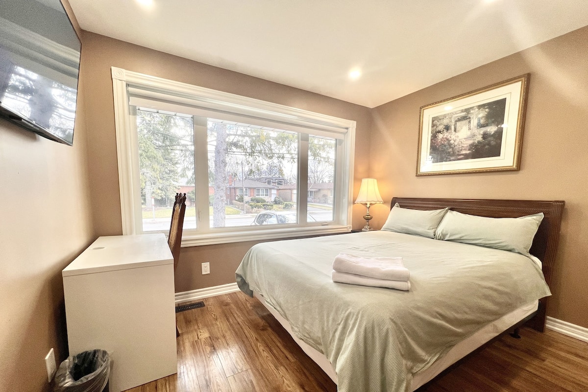 A bedroom with a bed, a nightstand, a lamp, a window, and a framed picture on the wall.