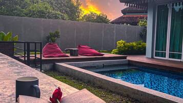 A serene outdoor setting with a swimming pool, a book, a rose, and a mug on a table.