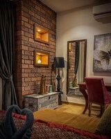 A cozy room with a brick wall, a wooden cabinet, a mirror, a red chair, and a bed with a patterned bedspread.
