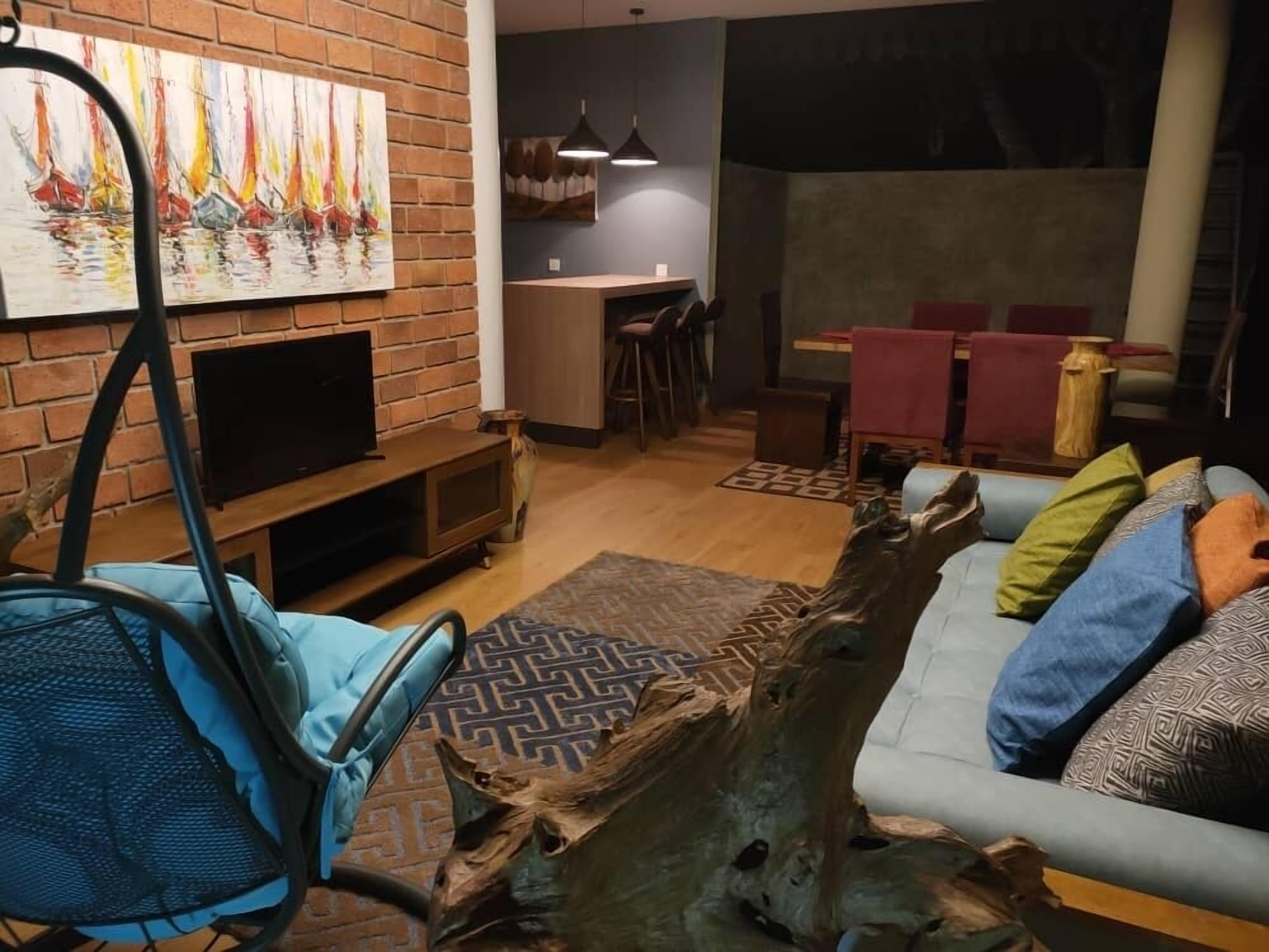 A living room with a brick wall, a TV, a dining area with a table and chairs, and a sofa with cushions.