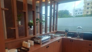 A buffet setup with various food containers and utensils, wooden cabinets, and potted plants. - Hotel Prime Classic (Hyderabad)