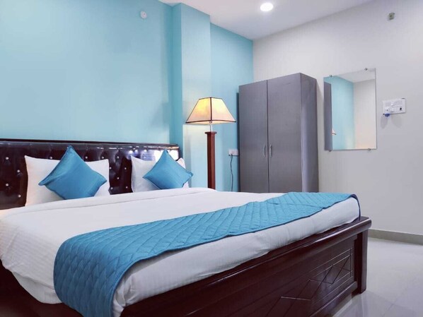 Una cama bien hecha con colcha azul, cabecera de madera oscura y almohadas azules.