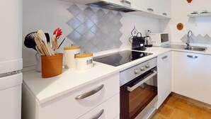 A modern kitchen with white cabinetry, a black stovetop, and a built-in oven. There are two white cabinets with silver handles, a stainless steel sink, and a small countertop with a kettle and a toaster.