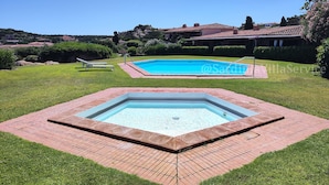 A swimming pool with a hot tub, surrounded by a well-maintained lawn and a view of houses in the background.